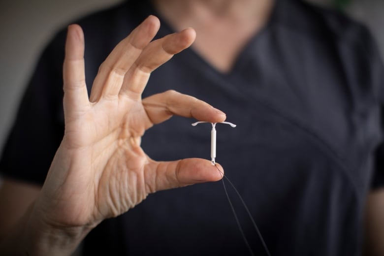 A doctor holds up a tiny T-shaped metal object, an intrauterine device (IUD)