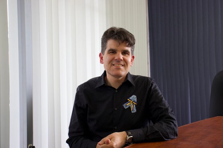 A man in a black shirt sits at a conference room table. 