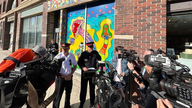 Two uniformed police officers are surrounded by media holding cameras and microphones.