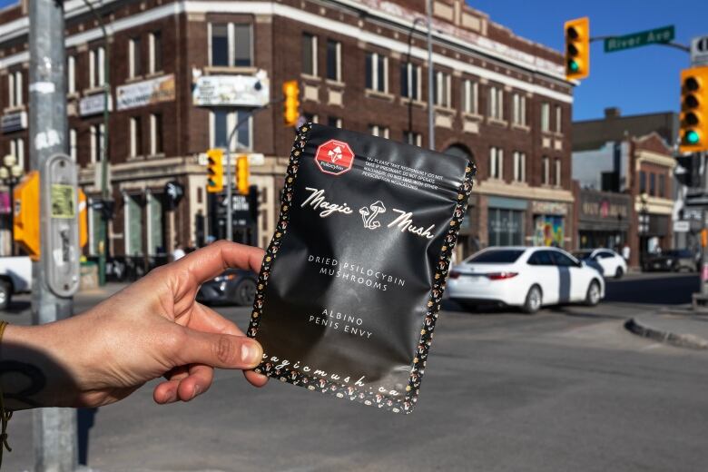 A black package labeled Magic Mush is held up in front of a busy intersection.