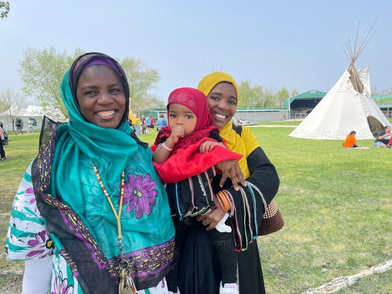 A mother, daughter and granddaughter are pictured smiling toward the camera. Behind them is a tipi.