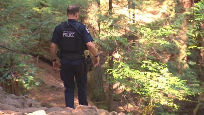 A uniformed police officer walks on a forest path.