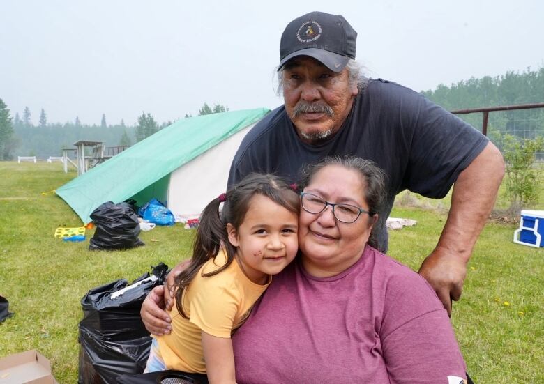 A man, a woman and a young girl pose in front of a tent