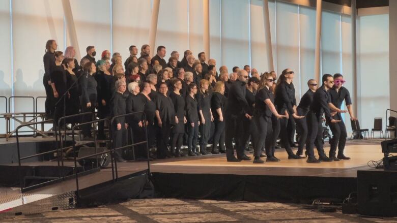 A chorus dressed in black performs on stage.