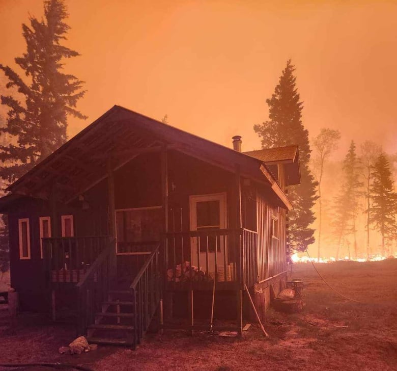 Wildfire surrounds wooden cabin.