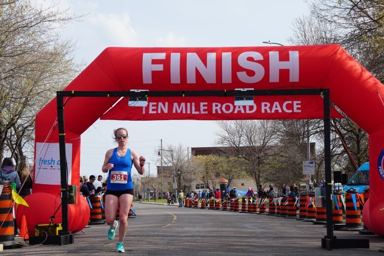 A runner in a blue shirt crosses under a red blow up finish point of a race. 