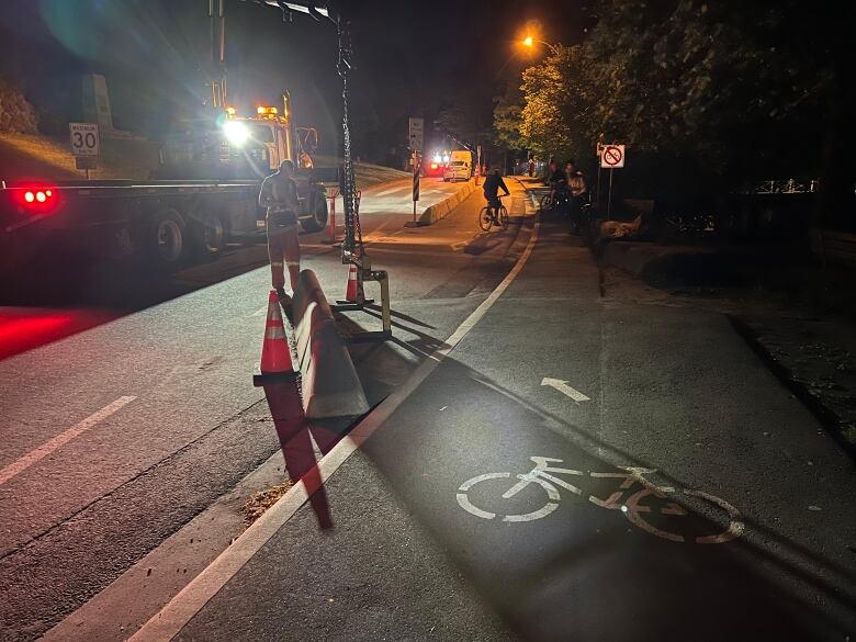 A worker is pictured monitoring as a machine prepares to lift up a concrete barrier slab between a road and bike lane. 