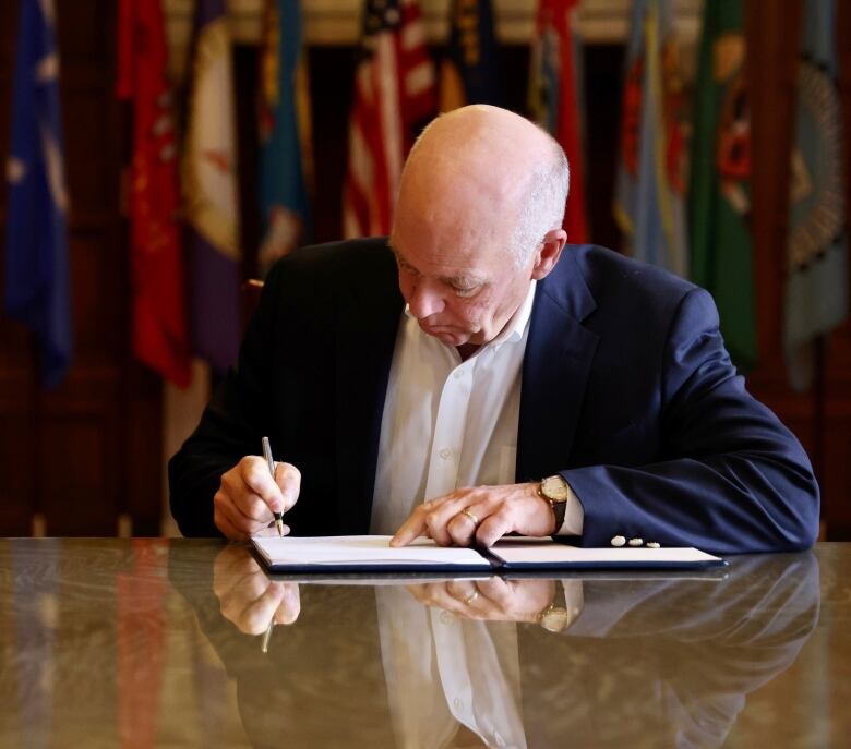 A bald man signs a document using a pen.