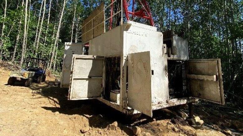 The entrance to a mining project stands on a dirt ground in front of trees.