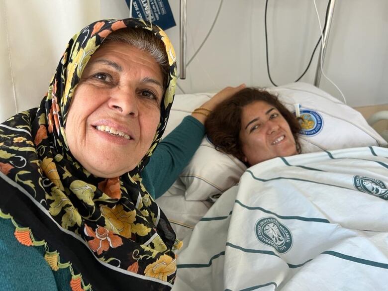 A person places their hand on the head of another person lying in a hospital bed.