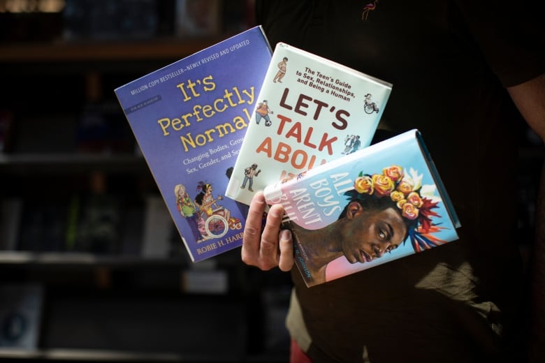 A man holds three books fanned out in his hand.