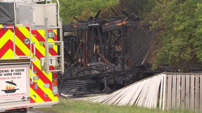 A fire truck with red and yellow stripes is seen parked next to the burned remnants of a house.