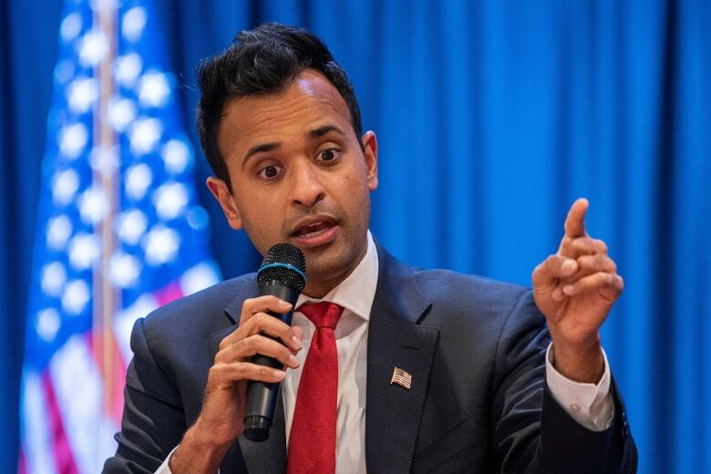 Dark haired man in dak jacket and red tie speaking into a microphone