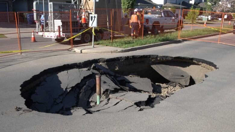 A road with a sinkhole and a man in the background is pictured.