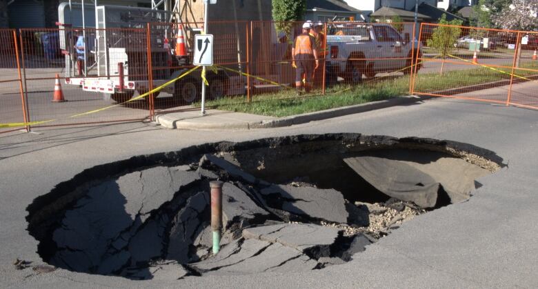 A road with a sinkhole and a man in the background is pictured.