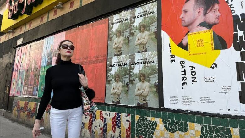 Woman in sunglasses in front of boarded up building on downtown street.