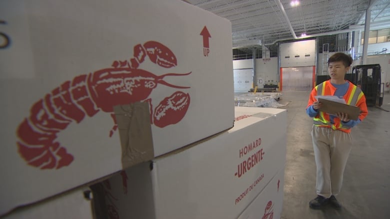 A man wearing a safety vest holds a clipboard. He is standing near boxes of lobster in a warehouse .