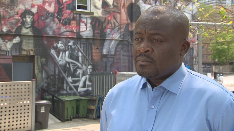 Man in blue shirt stands in front of a mural.