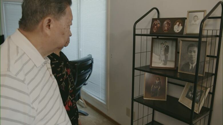 A person's back is to the camera and they are looking at older black and white photographs on a shelf.