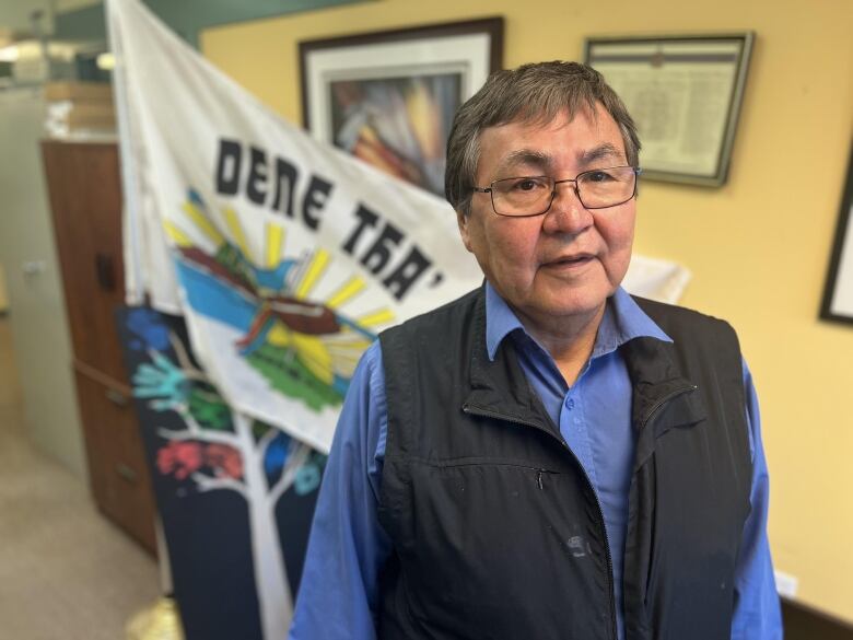 Chief Wilfred Hooka-Nooza of the Dene Tha' First Nation stands before the nation's flag.