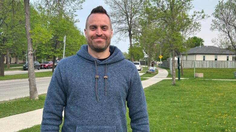 A man in a blood hoodie standing on grass with a sidewalk behind him.