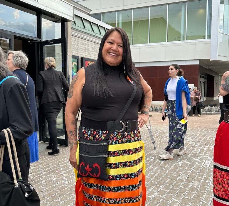 A smiling woman wearing a colourful skirt stands in a crowd of people.