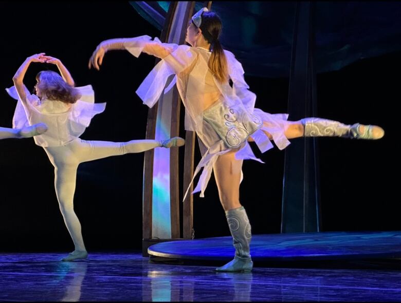 Two ballet dancers twirl on a blue stage.