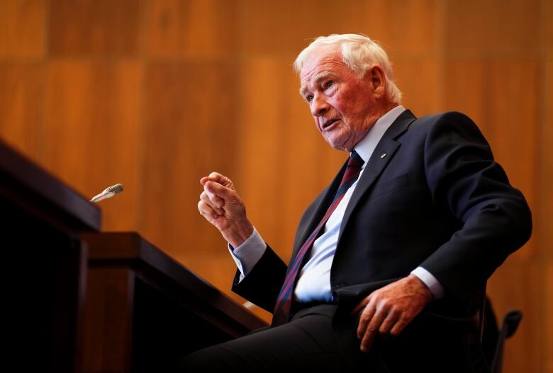 This profile photo show former Governor General David Johnston sitting in a chair speaking to reporters. 