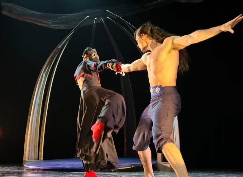 Two ballet dancers hold hands on a stage.