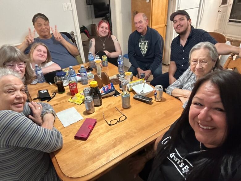 A family sits around a wooden table with water bottles and pop cans on it.