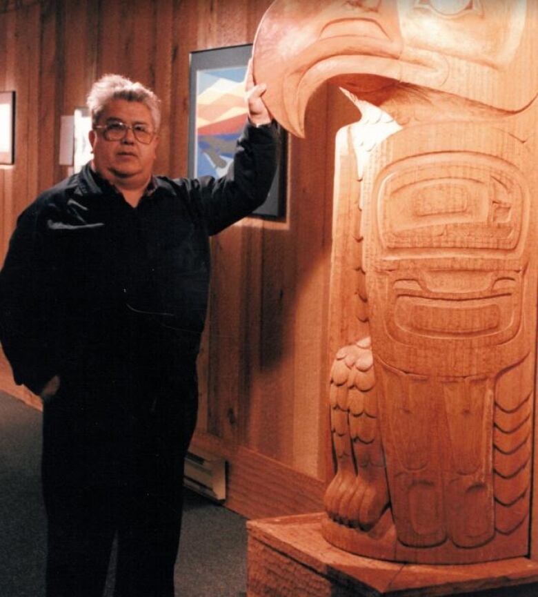 A man stands next to a totem pole