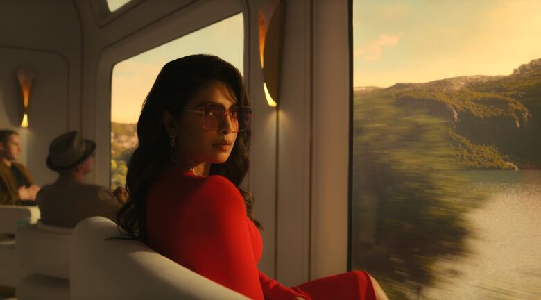 A woman wearing a red dress and sunglasses is shown on a train.