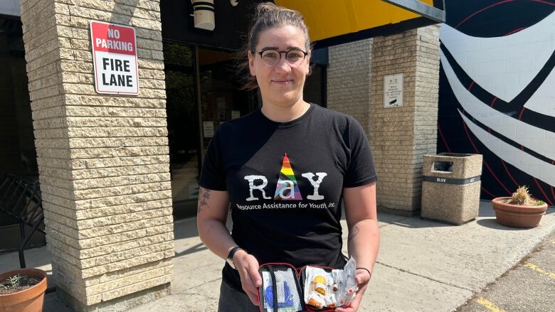 A woman wearing a black shirt that says RaY holds a kit filled with vials and needles. 