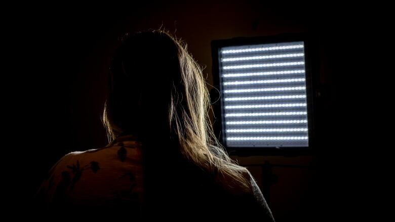 The back of a woman's silhouette is backlit with a bright light.