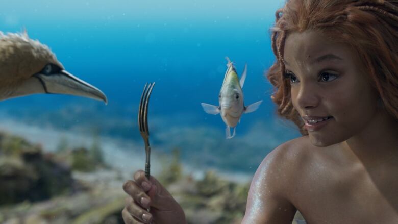 A woman with red hair, on the far right, is holding a fork in her hand. To her left is a hyper realistic CGI fish, and a bird. They are all underwater.