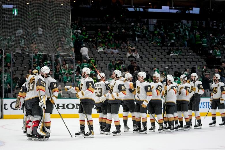 A hockey team wearing black, white and gold jerseys celebrate by hugging each other on the ice.