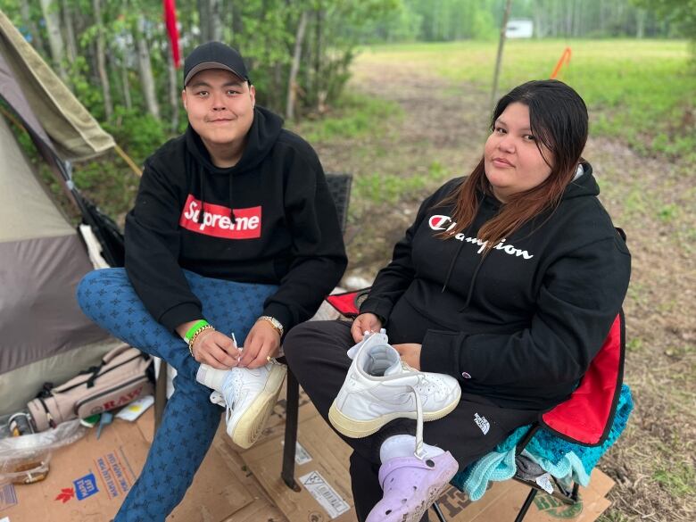 An Indigenous man and woman sit on camping chairs in front of a tent outdoors.