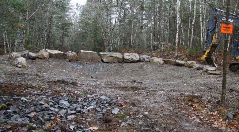 An area surrounded with trees is covered in dirt, rocks and gravel, with an excavator resting nearby.