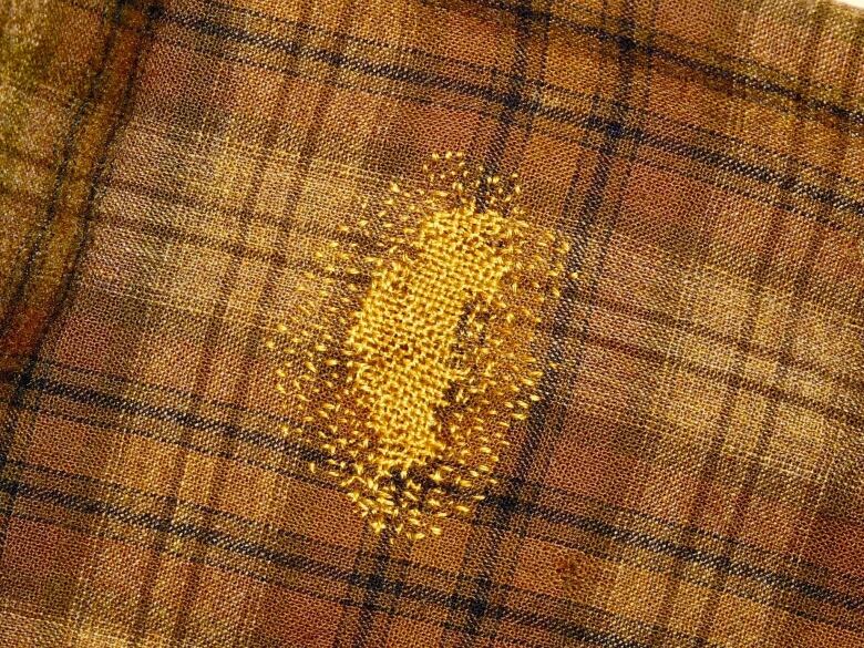 A brown plaid fabric is pictured with a smattering of gold fabric in a circle. 