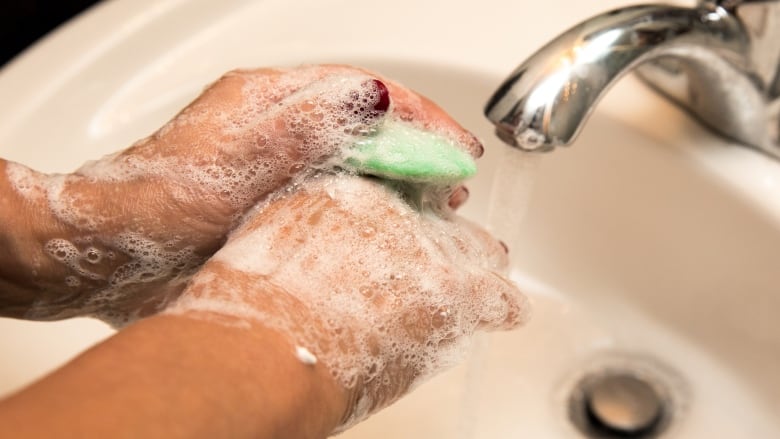 Hands covered in foam hold a green bar of soap in the sink