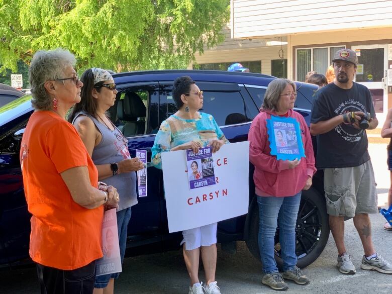 Four women and a man, some holding posters, one of which says Justice for Carsyn, lean against a dark SUV.