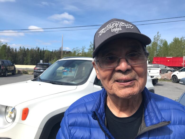 Man in blue coat, black ball cap and with glasses looks at camera.