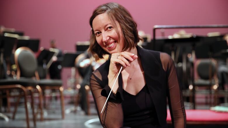 A lady in a black dress holds a conductor stick 