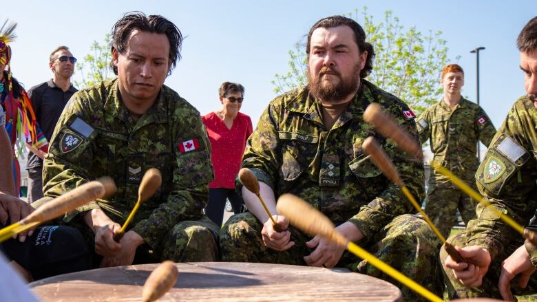 Men play an Indigenous drum as people hold hands dancing in a circle around them.