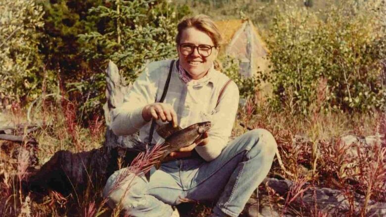 A woman poses holding a fish.