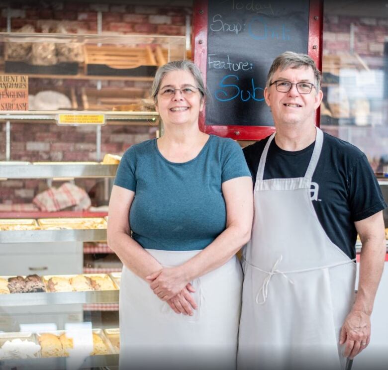 two people wearing aprons stand in front of bakery cases