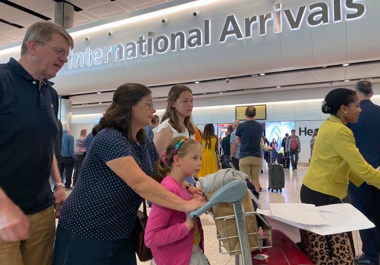 A family pushes luggage through a busy airport.