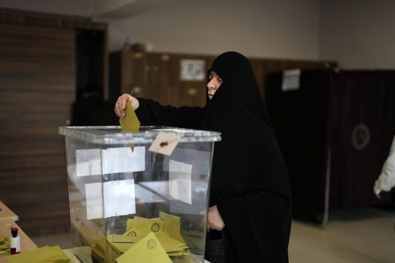 A person casts a ballot into a box at a polling station.