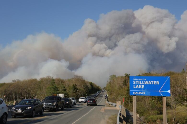 A line of cars heading away from a large plume of smoke.