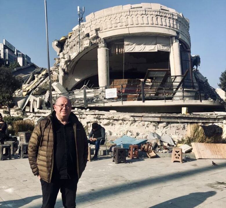 A man stands in front of a damaged building.